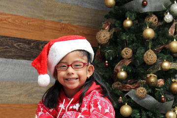 4-year-old Latina girl with brown hair and glasses celebrates Christmas and New Year's by opening presents under the tree