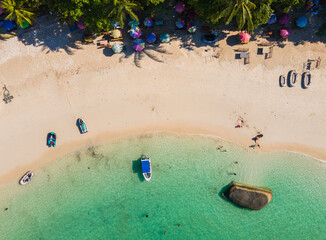 Stunning top-down aerial view of tropical Tanjung Tinggi beach in Belitung, Indonesia. Features clear turquoise water, giant granite boulders, boats, and colorful umbrellas.