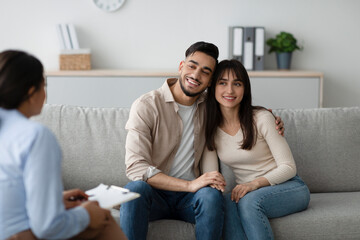 In a warm therapist's office, an Arab couple sits on a couch hugging and smiling after a productive therapy session. They are engaged and sharing their feelings with the psychologist.