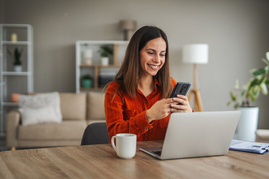 Woman smiling using smart phone and laptop working from home - Powered by Adobe