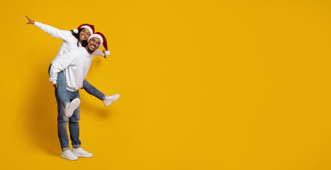 A joyful couple expresses their holiday spirit by posing playfully in festive hats. The bright yellow backdrop enhances their cheerful mood and celebration of the season.