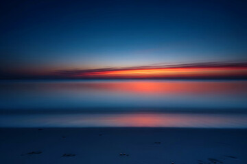 Deep blue twilight over smooth sea with orange glow on horizon, long exposure minimal seascape ideal as tranquil background for design projects.