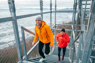 Two bright red and yellow sporty clothes dressed men running up on huge steel industrial stairs in cold winter day. Men's friendship and healthy lifestyle concept photo.