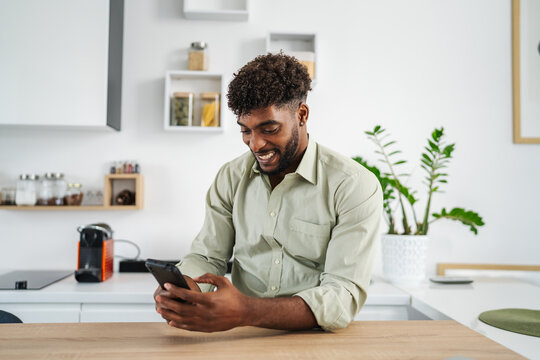 Young black man smiling using smart phone in kitchen