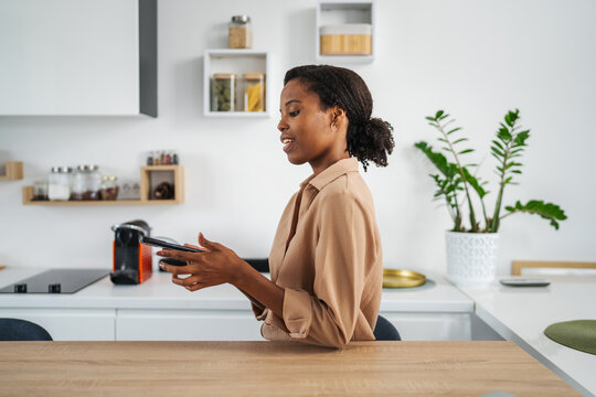 Young african american woman socializing on smart phone in kitchen