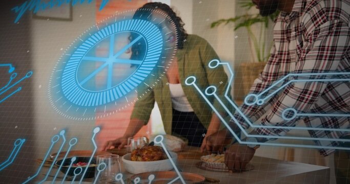 Leaning couple wearing plaid shirt and green jacket arranging roast chicken at home table, blue HUD - Powered by Adobe