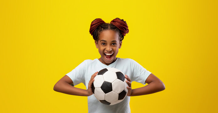 A cheerful young girl with braided hair smiles broadly while holding a black and white soccer ball. The vibrant yellow background enhances her joyful expression and energy. - Powered by Adobe