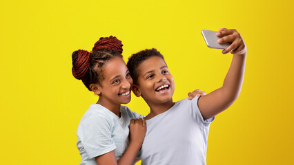 Two children are happily posing for a selfie, with one leaning on the other. They are smiling...