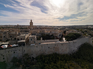 Fototapeta premium High altitude aerial view of Mdina old town at sunset, the Silent City with yellow limestone walls and St. Paul's Cathedral, scenic drone shot in Malta.