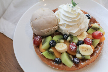 Waffles with strawberry, kiwi, banana and whipping cream in white plate on sheer curtain. Morning breakfast, dessert.