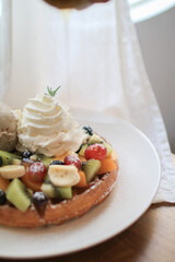 Waffles with strawberry, kiwi, banana and whipping cream in white plate on sheer curtain. Morning breakfast, dessert.