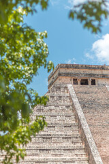 Fototapeta premium Chichen Itza pyramid framed by blurred tree in the foreground, Yucatan, Mexico