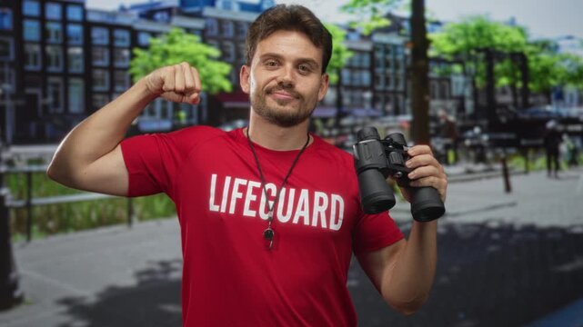 Man lifeguard flexing biceps wearing red shirt and holding binoculars on amsterdam street; confidence rescue readiness.