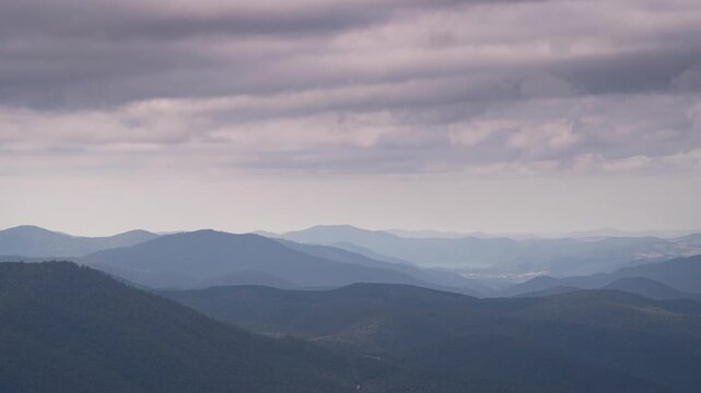 Time lapse of grey clouds moving across the sky with patterns of sunlight passing over blue mountains below,