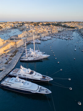 High angle aerial view of traditional boats and luxury yachts in crystal clear turquoise water, scenic Mediterranean coast of Malta, sunny summer travel destination