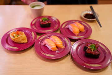 Assorted sushi on red plates including salmon nigiri, tuna gunkan, and inari.