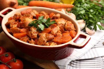 Delicious cooked stew in baking dish and fresh ingredients on table, closeup