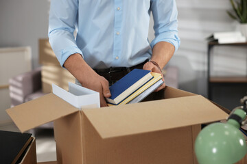 Moving day. Man putting books into cardboard box at table in office, closeup