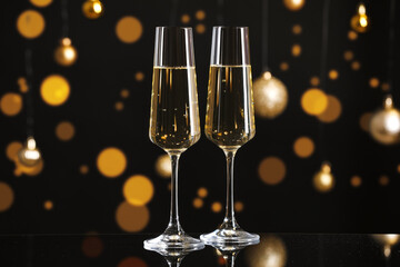 New Year celebration. Sparkling wine in glasses on mirror table and festive decor against black background