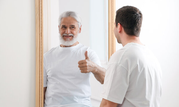 Young man seeing himself as senior man in mirror. Concept of personality, past and future, flow of time, age