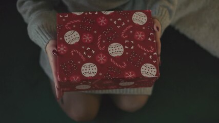 A close-up view of a wrapped Christmas gift box featuring red paper with white ornaments, candy canes, and snowflake patterns. The cozy holiday theme evokes warmth, joy, and the spirit of giving. - Powered by Adobe
