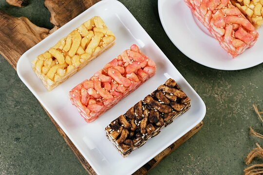 Three colorful sachima blocks arranged on a wooden tray. Bright, clean food image for snack or dessert themes.