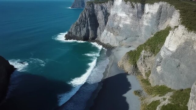 Impresionante vista a&eacute;rea de acantilados costeros escarpados y playa de arena oscura con olas rompiendo en un d&iacute;a soleado.