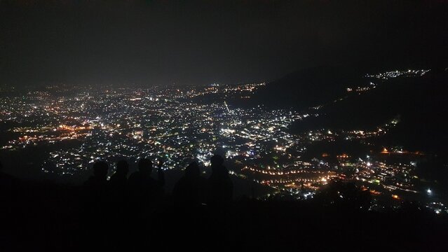 Night view of Batu City from Paralayang hill with glowing city lights and silhouetted people standing in the foreground, capturing urban life and reflection