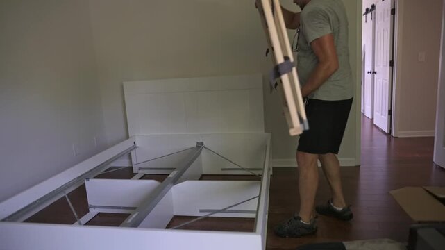 man building bed, man assembling bed frame carefully, homeowner organizing bed using tools and measurements, individual constructing bed frame in room with precise effort and casual attire