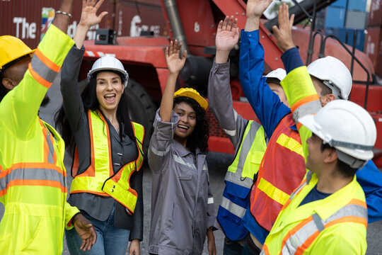 Diverse group of industrial container workers celebrating success with clapping hands at shipping yard, showing teamwork, motivation and positive collaboration in logistics operations.