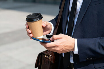 A businessman in suit holding coffee cup and smartphone while being outdoors, representing modern work life.