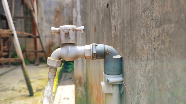 A close-up of a hand turning on an outdoor water faucet, with clean water flowing before being turned off again, symbolizing water conservation, daily life, and environmental awareness.