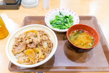 A Japanese beef bowl set meal from Sukiya, featuring simmered sliced beef over steamed rice, served with fresh vegetables and side dishes. The presentation highlights traditional Japanese fast food wi