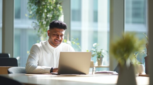 Smiling indian business man working on laptop at home office. Young indian student or remote teacher using computer remote studying, virtual training, watching online education webinar at home office