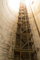 Bottom up view of a vertical mine shaft of Sinking manhole with concrete Wall Friction Staircase safety with net fall-protection in underground construction site or fire escape, a ladder or stairway.