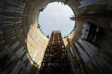Fototapeta premium Bottom up view of a vertical mine shaft of Sinking manhole with concrete Wall Friction Staircase safety with net fall-protection in underground construction site or fire escape, a ladder or stairway.