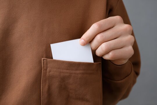 close-up of a hand taking out a white sticker with an empty space for text from a brown sweatshirt pocket. this is a mockup template of a blank label inside a sleeve, shown in close-up.