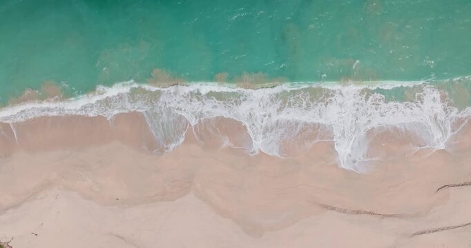 Top down turquoise ocean waves breaking shore, white foam crashing pristine, light colored sand of a picturesque tropical beach on the tropical Lombok island, Indonesia. Aerial view natural bavkground