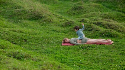 Caucasian woman doing yoga with her little son outdoors. 
