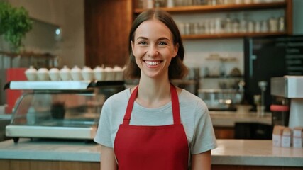 Woman in red apron leaning slightly forward, smiling confidently, illuminated restaurant menu board and decorative hanging lights visible, interior cozy and modern - Powered by Adobe