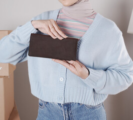 Young woman's body in a knitted sweater and jeans and her hand showing an elegant matte brown leather purse