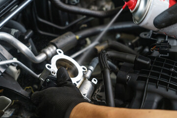 Obraz premium Auto mechanic cleaning a vehicle's throttle body. Technician uses a spray cleaner for engine maintenance in a repair shop.