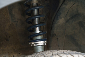 Detailed close-up of a dirty adjustable coilover suspension and spring mounted on a car. Automotive part and vehicle tuning concept. © christian vinces