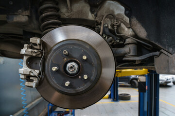 Detailed close-up of a car brake disc and caliper assembly in an auto repair shop. Vehicle...