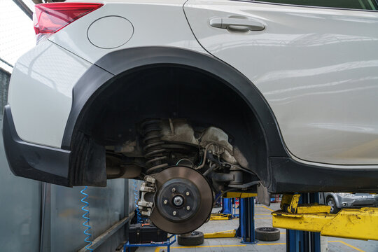 Close-up of a car's brake disc and suspension assembly. The vehicle is raised on a lift in an auto repair shop for maintenance or service. - Powered by Adobe