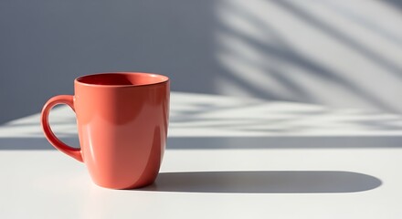 A single red mug sits on a white table with dappled light and shadow on the wall behind it