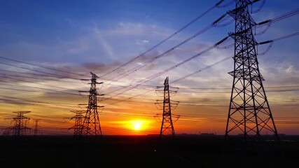 High voltage electricity pylons and power lines silhouetted against a beautiful orange sky during a vibrant sunset - Powered by Adobe