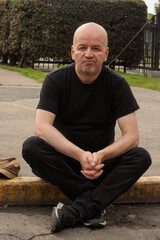 Casual bald man sitting on the curb outdoors