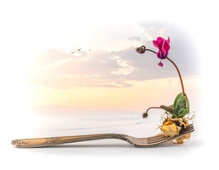 A delicate purple flower and stem sprout from a fork, with a soft sunset and birds in the dreamy background
