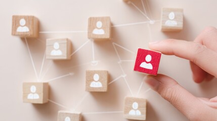 Strategic Connections: A hand carefully places a vibrant red block within a network of wooden cubes, each depicting a human icon, symbolizing the dynamics of connections and people.